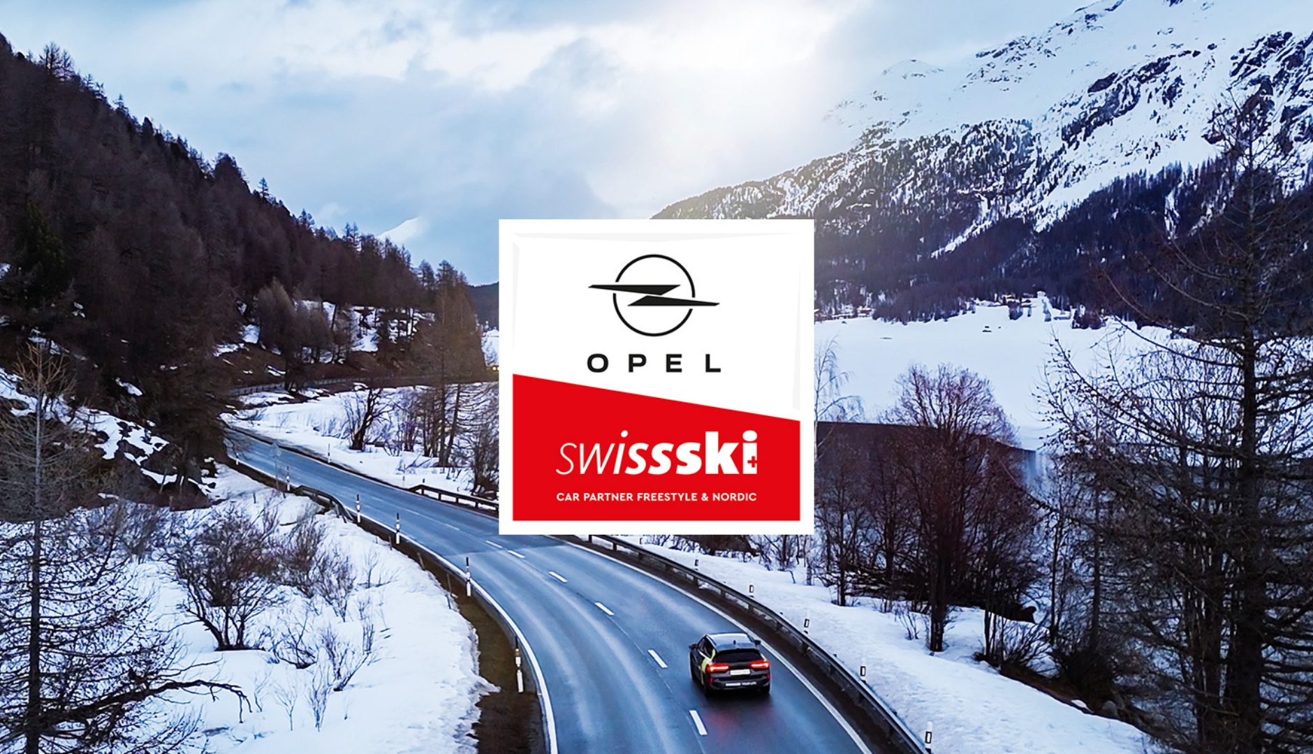 Auto auf schneebedeckter Strasse in den Bergen mit Opel und Swiss Ski Logos im Vordergrund.
