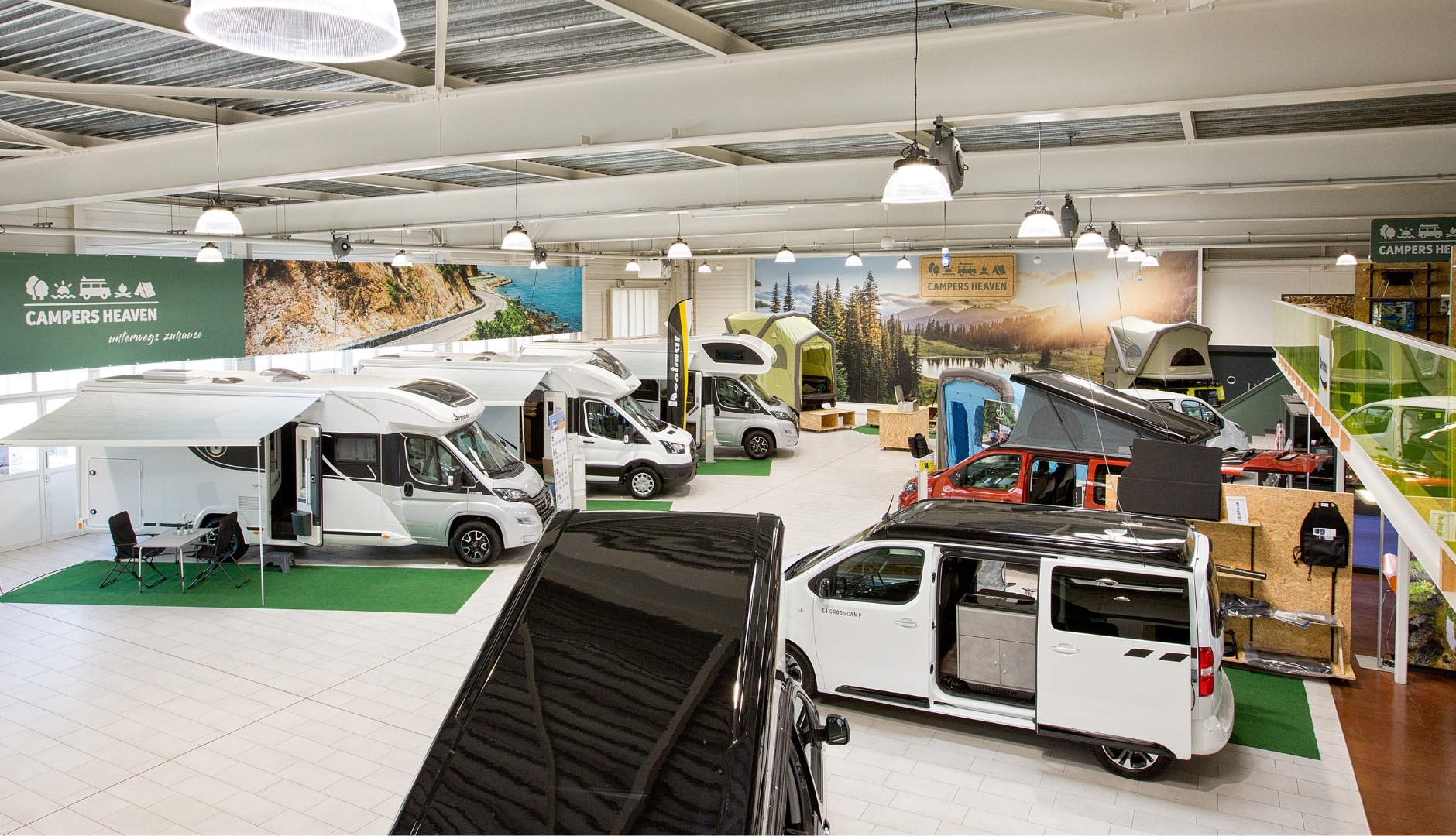 Innenansicht einer Camper-Ausstellungshalle mit mehreren Fahrzeugen unter dem Banner 'Campers Heaven'.
